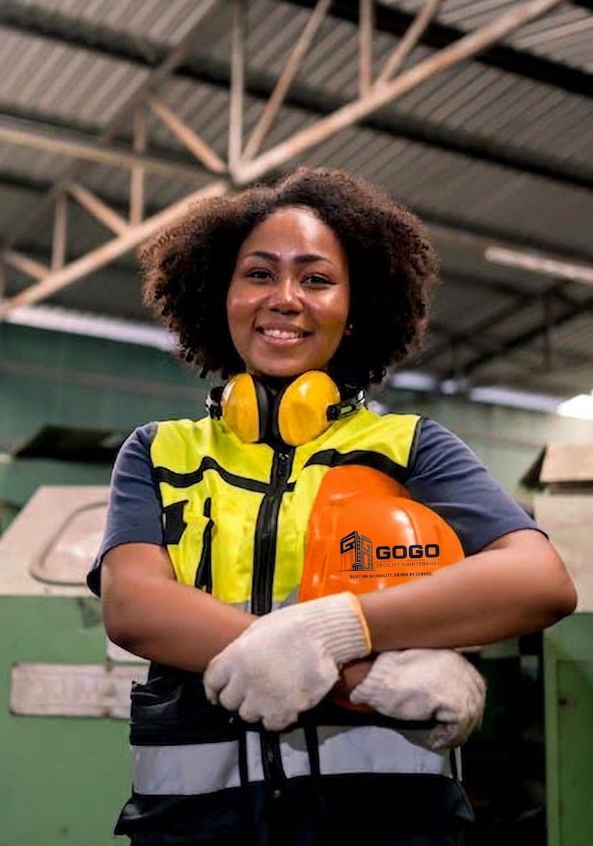 Smiling GOGO Facility Maintenance worker in a safety vest holding a branded hard hat